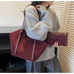 Detail of burgundy suede tote bag and matching clutch set in a minimalist studio setting
