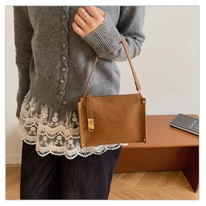 Détail du sac à bandoulière en daim marron avec fermoir doré et rivets décoratifs
