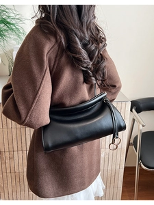 Dettaglio della borsa baguette in pelle nera lucida con eleganti anelli in metallo dorato