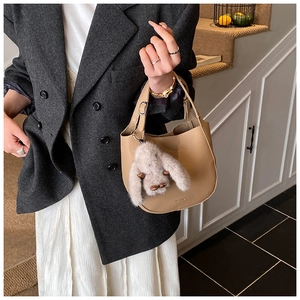 Detail of khaki leather bucket bag with litchi texture and cute rabbit charm ornament