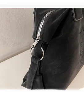 Detail of black leather tote bag featuring embossed patterns and silver metal zipper