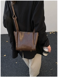 Detailansicht der braunen Leder-Eimertasche mit Logo-Prägung und goldenen Metallfüßen