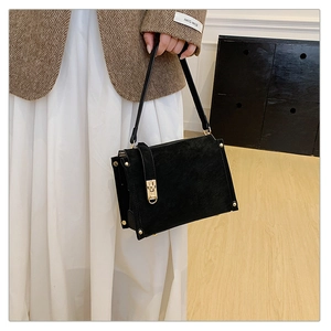 Détail du sac à bandoulière en daim noir avec rivets dorés et serrure sur un modèle