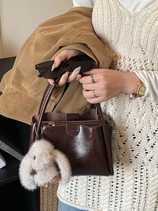 Brown patent leather handbag with plush charm shown in a stylish lifestyle setting