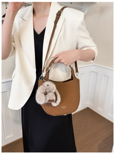 Close-up of brown leather bag with MUCQUU logo, rabbit charm, and adjustable shoulder strap