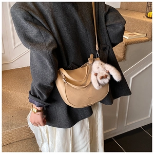 Detail of beige lychee pattern half-moon bag featuring a cute plush bunny pendant