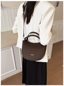 Detail of dark brown leather crescent bag showing textured finish and brand logo