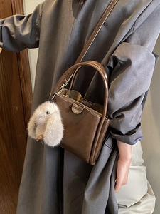Elegant brown leather top handle bag for women with a plush rabbit charm and shoulder strap