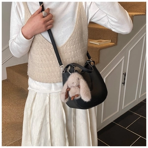 Detail of black lychee grain leather bucket bag with cute plush rabbit charm on strap