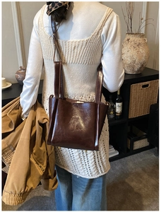 Frau trägt eine dunkelbraune Bucket Bag aus Ölwachsleder in einem warmen Interieur