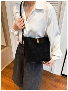 Détail d'un sac seau en cuir noir avec fermoir tournant doré sur un mannequin minimal