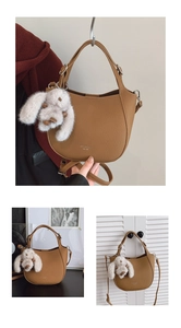 Detail of brown semi-circular handbag featuring a white plush rabbit charm and gold logo