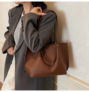Close-up of a large brown pebbled leather tote bag styled with a grey winter coat