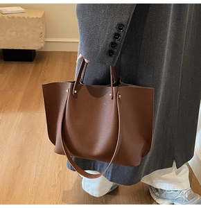 Detail of dark brown pebble leather tote bag featuring gold rivets and shoulder strap