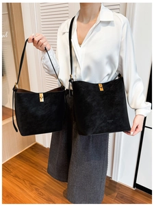 Détail du sac seau mat noir avec fermoir doré porté par un mannequin en chemise de soie