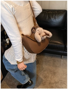 Brown lychee leather saddle bag with gold logo and plush rabbit charm detail