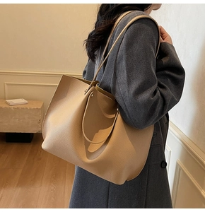 Beige pebble leather tote bag shown on model in a minimalist modern interior setting