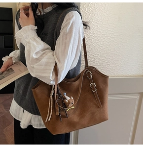 Detail of a large brown suede tote bag featuring adjustable straps and a cute bear charm
