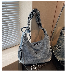 Detail of vintage washed blue denim hobo bag with ruffled strap and stylish side ruffles