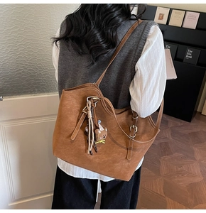 Brown tote bag in matte leather featuring a cute bear charm and adjustable shoulder strap