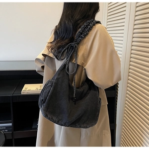 Detail of grey denim hobo bag with pleated shoulder strap and bow accent decoration