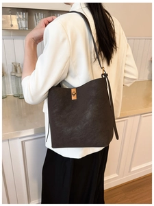 Détail du sac seau en cuir café avec fermoir doré sur un mannequin en costume blanc