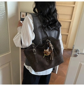 Detail of dark brown suede tote bag with white stitching and decorative charms