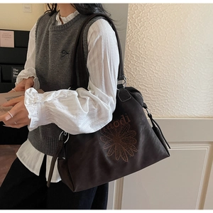 Détail d'un sac cabas marron foncé avec broderie florale et boucle en métal argenté