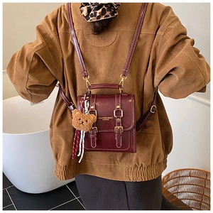 Gros plan du sac à dos en cuir bordeaux avec boucle dorée et breloque ourson