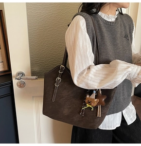 Detail of dark brown tote bag with bear charm and adjustable strap on model
