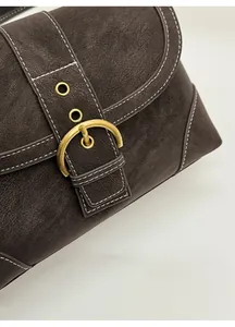 Detail of vintage brown suede bag featuring brass horseshoe buckle and white stitching