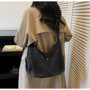 Detail of black washed denim hobo bag with pleated shoulder strap and metal logo