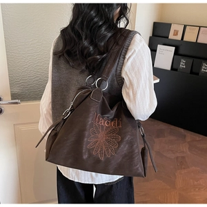 Close-up of brown tote bag with floral embroidery and metallic ring detail