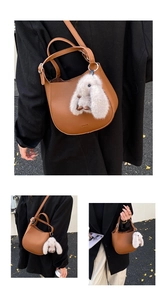 Detail of brown lychee leather bucket bag with plush bunny charm on autumn pavement