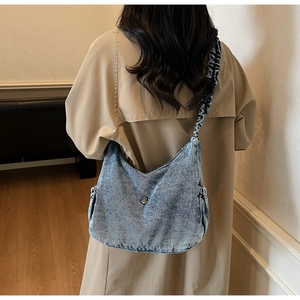 Detail of light blue denim crossbody bag with ruched shoulder strap and metal buckle