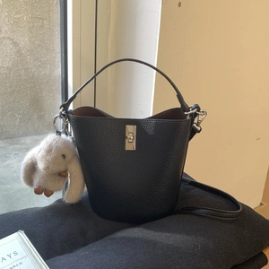 Détail d'un sac seau noir texturé avec fermoir rotatif argenté et breloque lapin en peluche