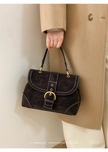 Detail of dark suede handbag featuring contrast stitching and a gold ring buckle