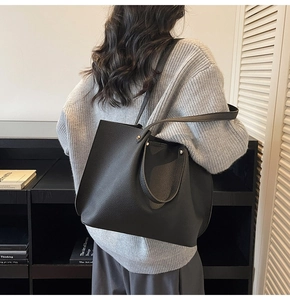 Detail of black pebbled leather tote bag with rivets and dual straps on model shoulder