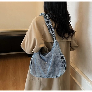 Detail of blue denim shoulder bag showing ruffled strap and silver M logo on beige coat