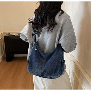 Detail of blue denim hobo bag with M-logo emblem and adjustable wide shoulder strap