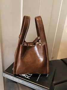 Retro dunkelbraune Beuteltasche mit HOCOMU-Logo auf modischen Büchern platziert
