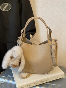 Elegant khaki lychee leather bucket bag with plush rabbit charm on a minimalist background