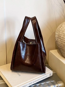 Dunkelbraune Handtasche aus Ölwachs-Leder im Retro-Stil auf einem silbernen Koffer