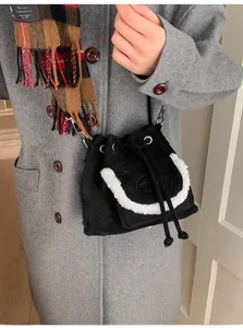 Close-up of black suede bucket bag with white faux shearling trim on grey wool coat