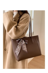 Detail view of dark brown pebbled tote bag with printed silk scarf on a camel coat