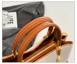 Détail de la poignée en cuir marron caramel avec boucles dorées et coutures contrastées