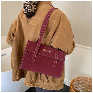 Detail of burgundy leather tote showing contrast stitching and gold logo plate hardware