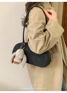 Close-up of minimalist black baguette bag with white rabbit plush charm on beige trench coat