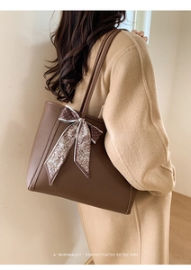 Detail of dark brown lychee leather tote bag with silk scarf on handle on model