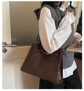 Detail of dark brown leather tote bag with silver buckle strap in a minimalist setting